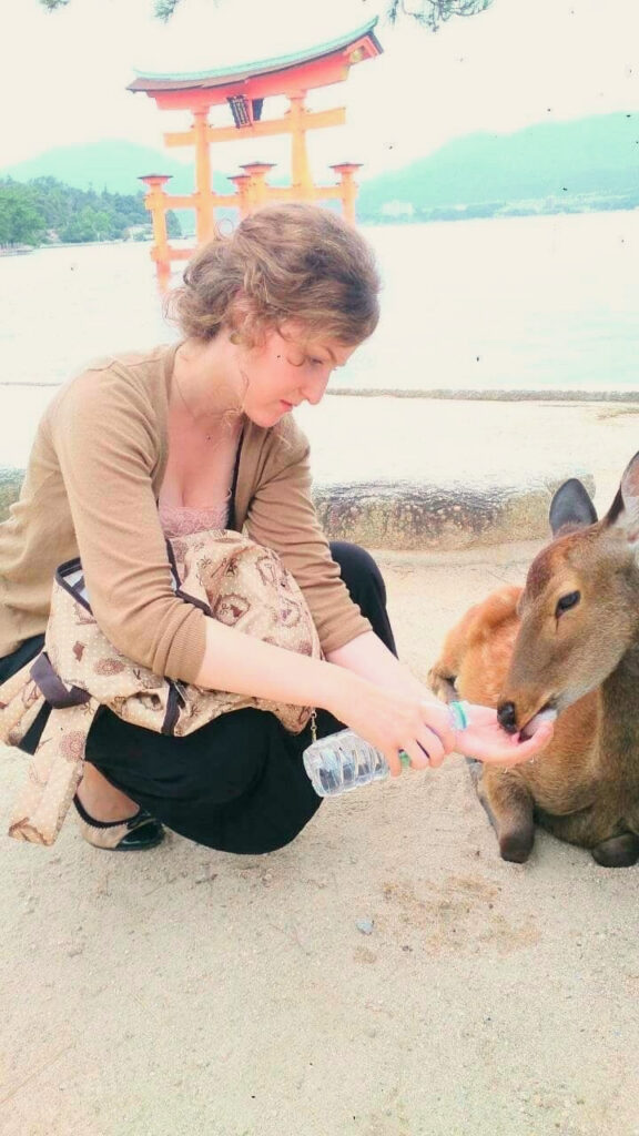 Clémentine Coutantic crouching beside a deer near a red torii gate in Japan
